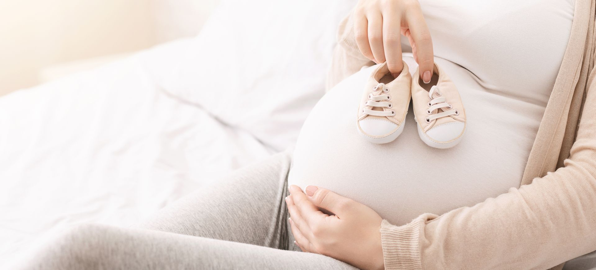 Uma mulher grávida está segurando um par de sapatos de bebê na barriga.