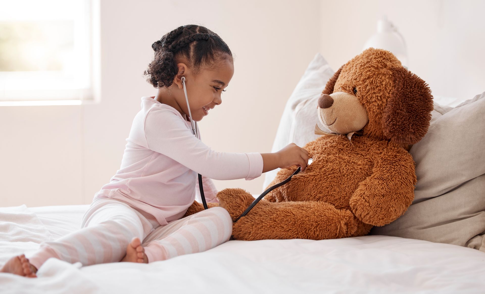 Uma menina está brincando com um ursinho de pelúcia com um estetoscópio.