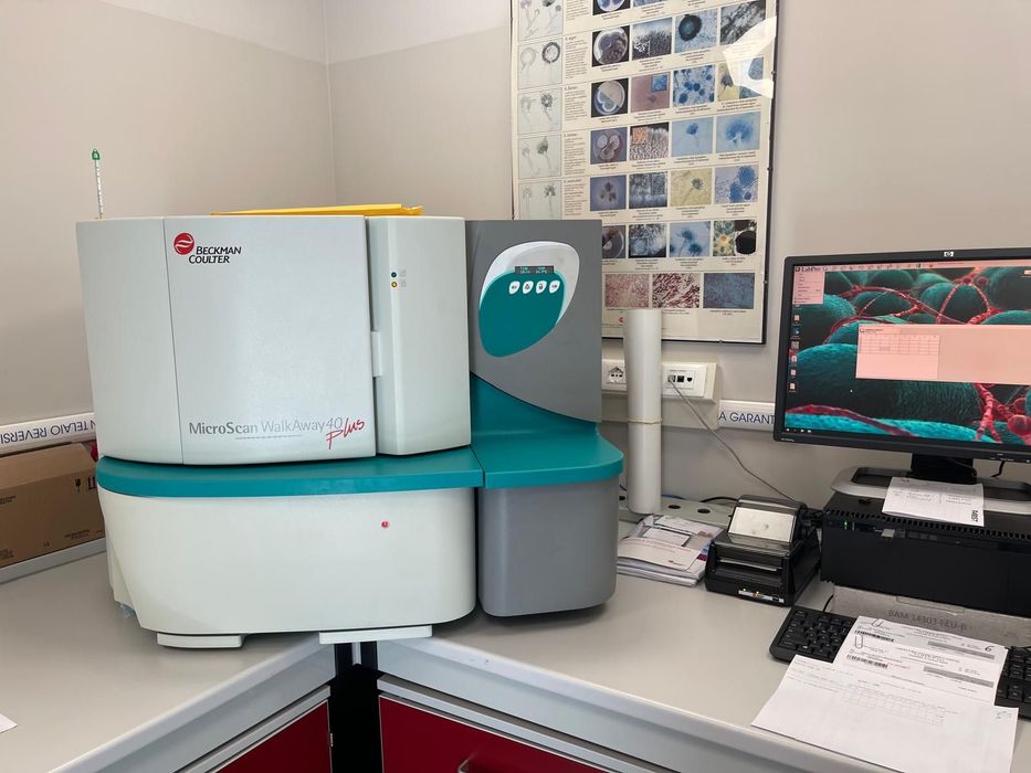 Strumento di laboratorio da tavolo su una scrivania accanto a un monitor che visualizza grafici e stampe di dati.