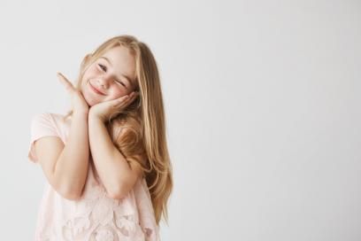 Une petite fille sourit avec ses mains sur son visage.