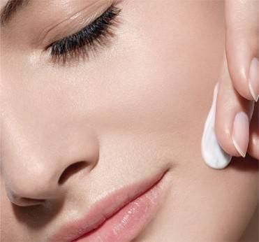 Gros plan d'une femme appliquant de la crème sur son visage.