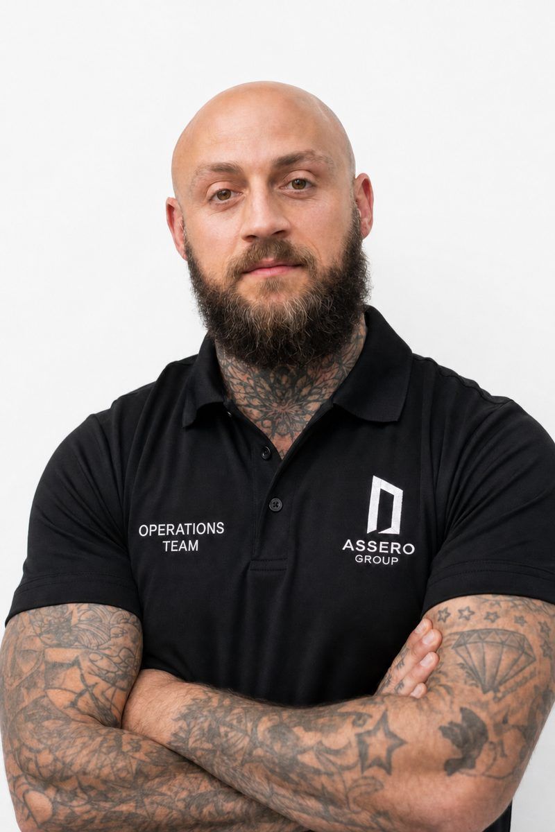 Smiling person with tattoos on both arms wearing a black polo shirt with a 