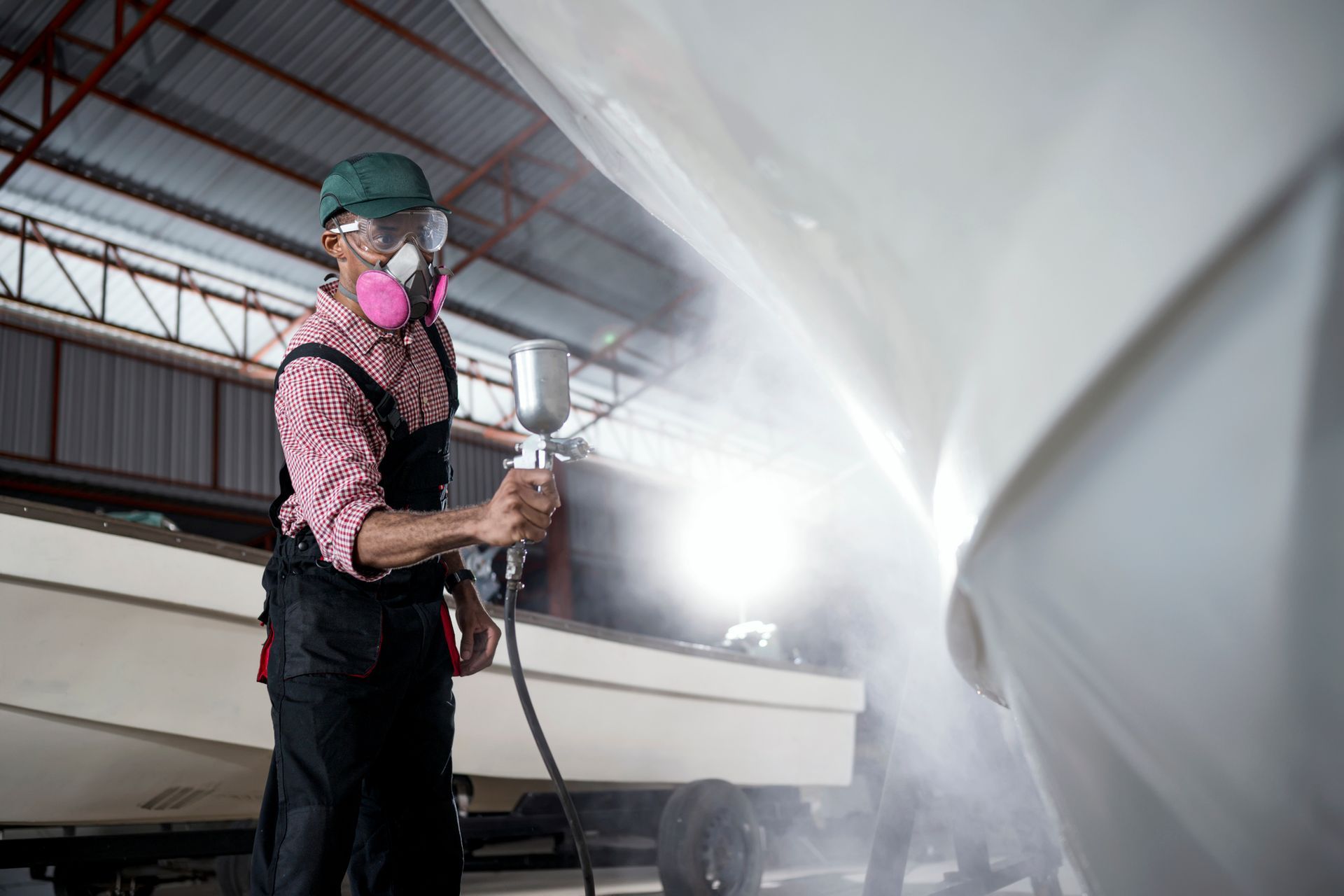 A man is spray painting a boat in a garage - Portland, OR - Drew Paints Inc.