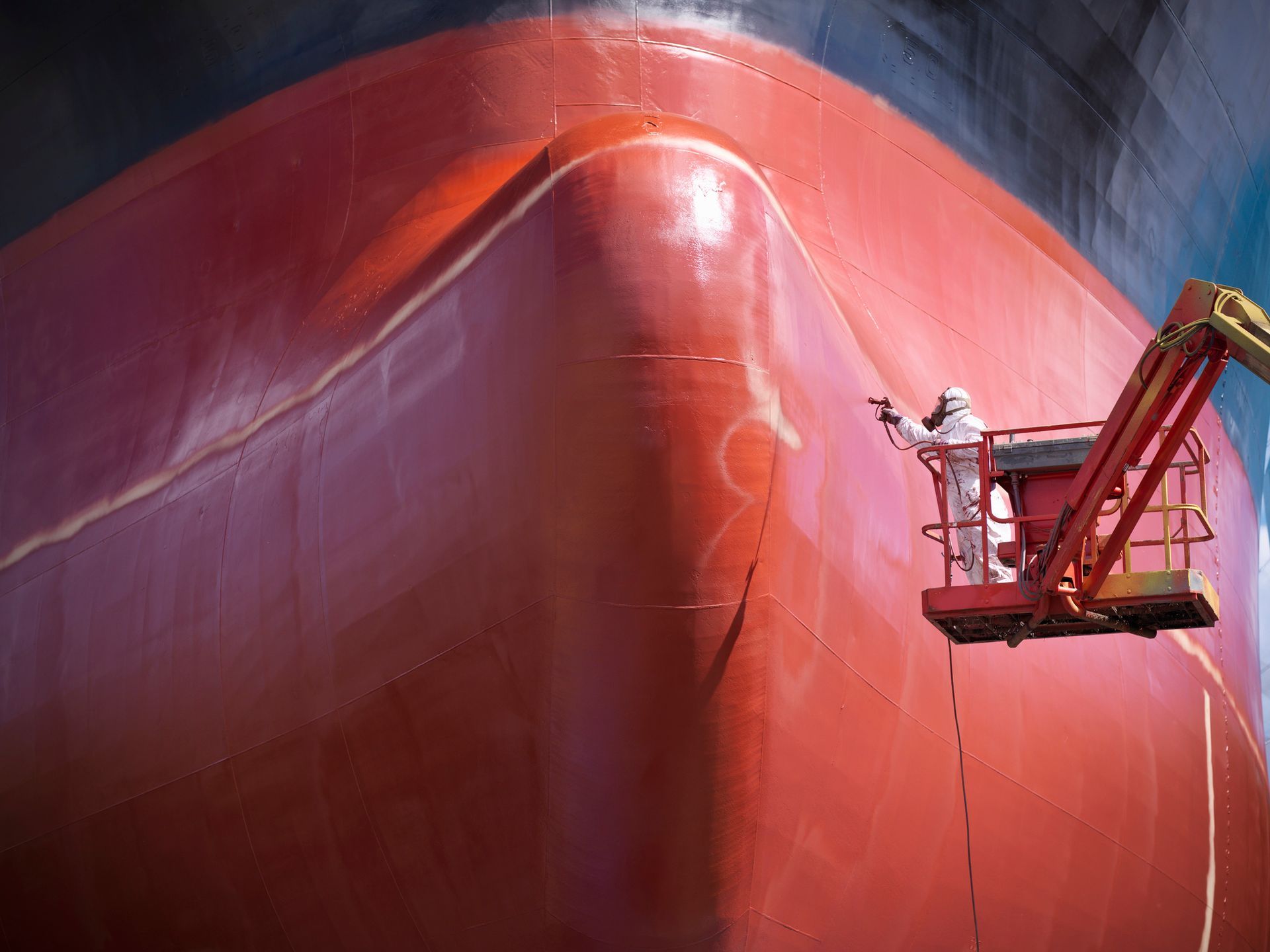A man is painting the bow of a large red ship - Portland, OR - Drew Paints Inc.