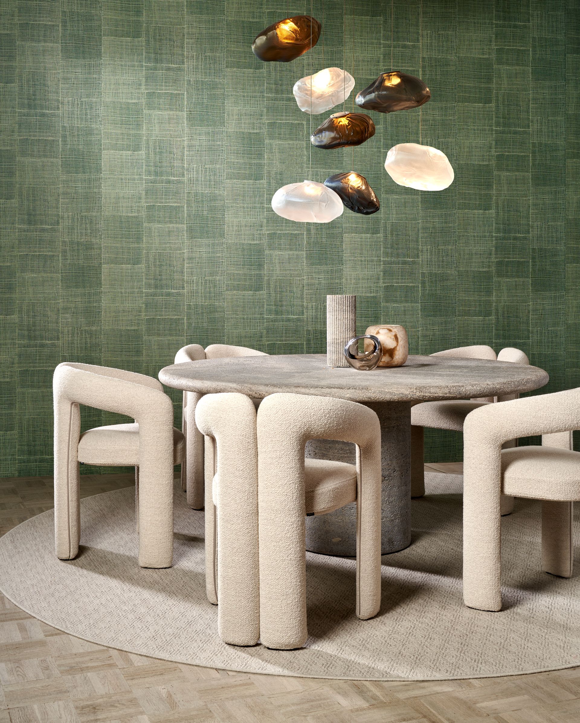 Sala da pranzo con sedie beige, tavolo in pietra e lampada a forma di nuvola contro una parete verde testurizzata.
