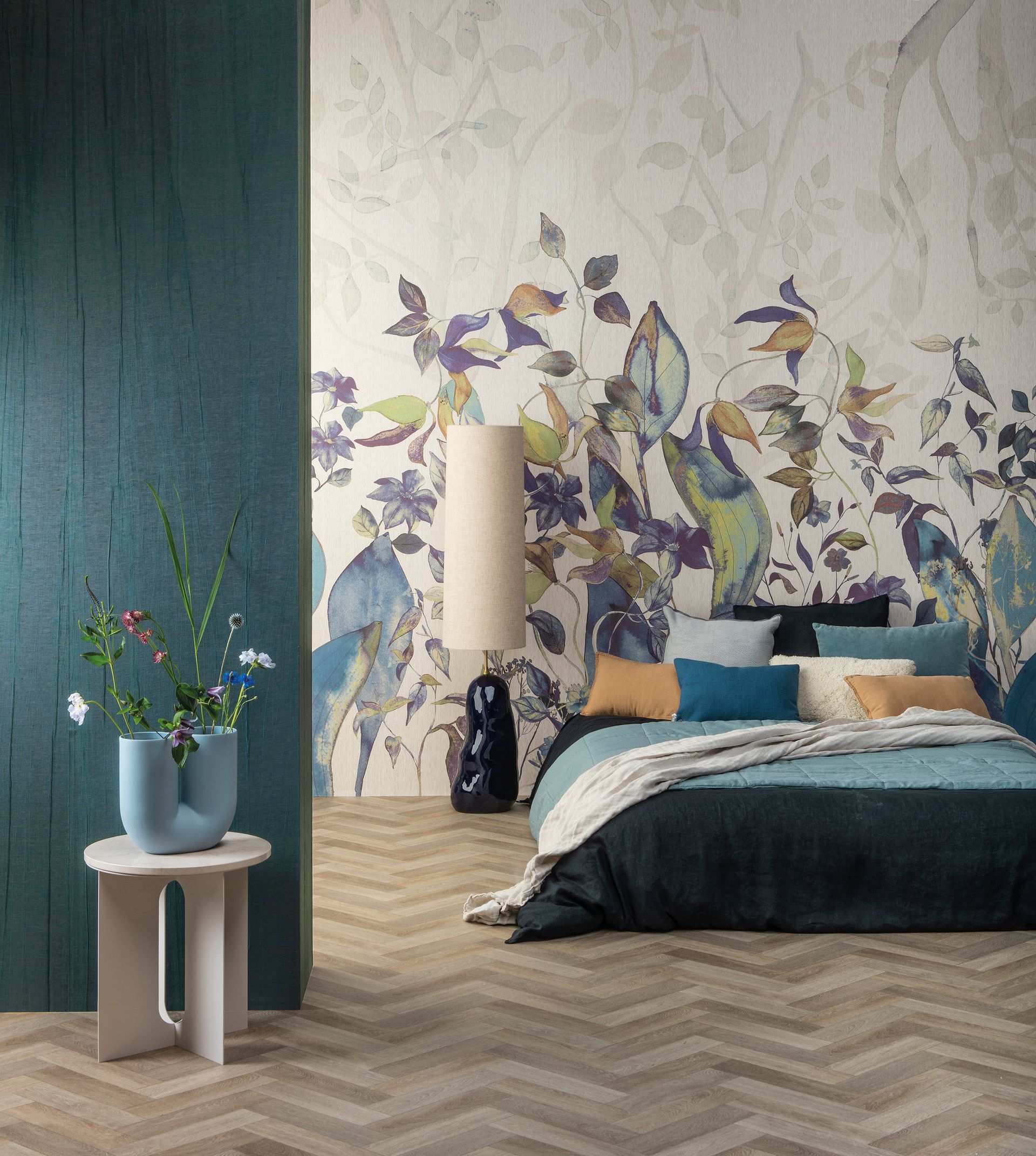Camera da letto con carta da parati floreale, dettagli color verde acqua, letto, vaso di fiori e pavimento in legno.