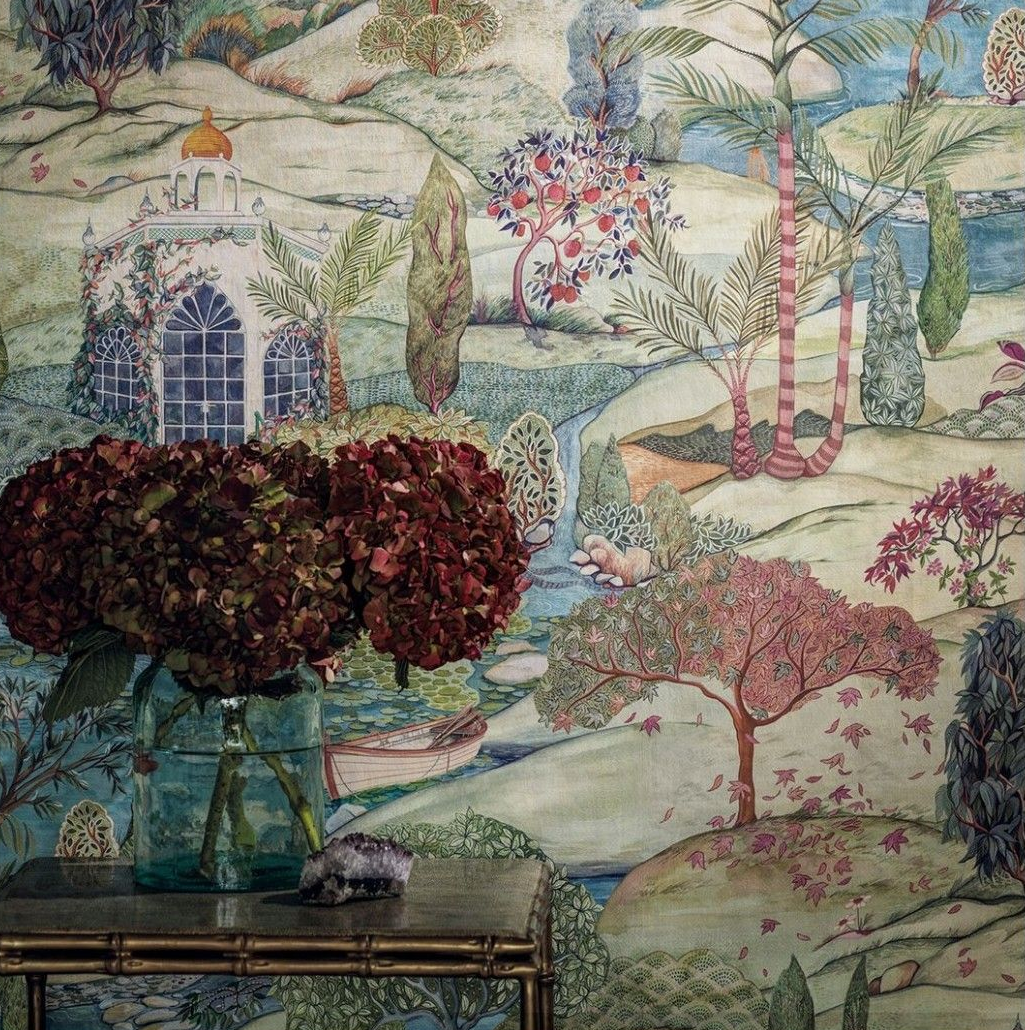 Fiori in un vaso su un tavolo con uno sfondo di carta da parati panoramica raffigurante un paesaggio con alberi e un edificio.