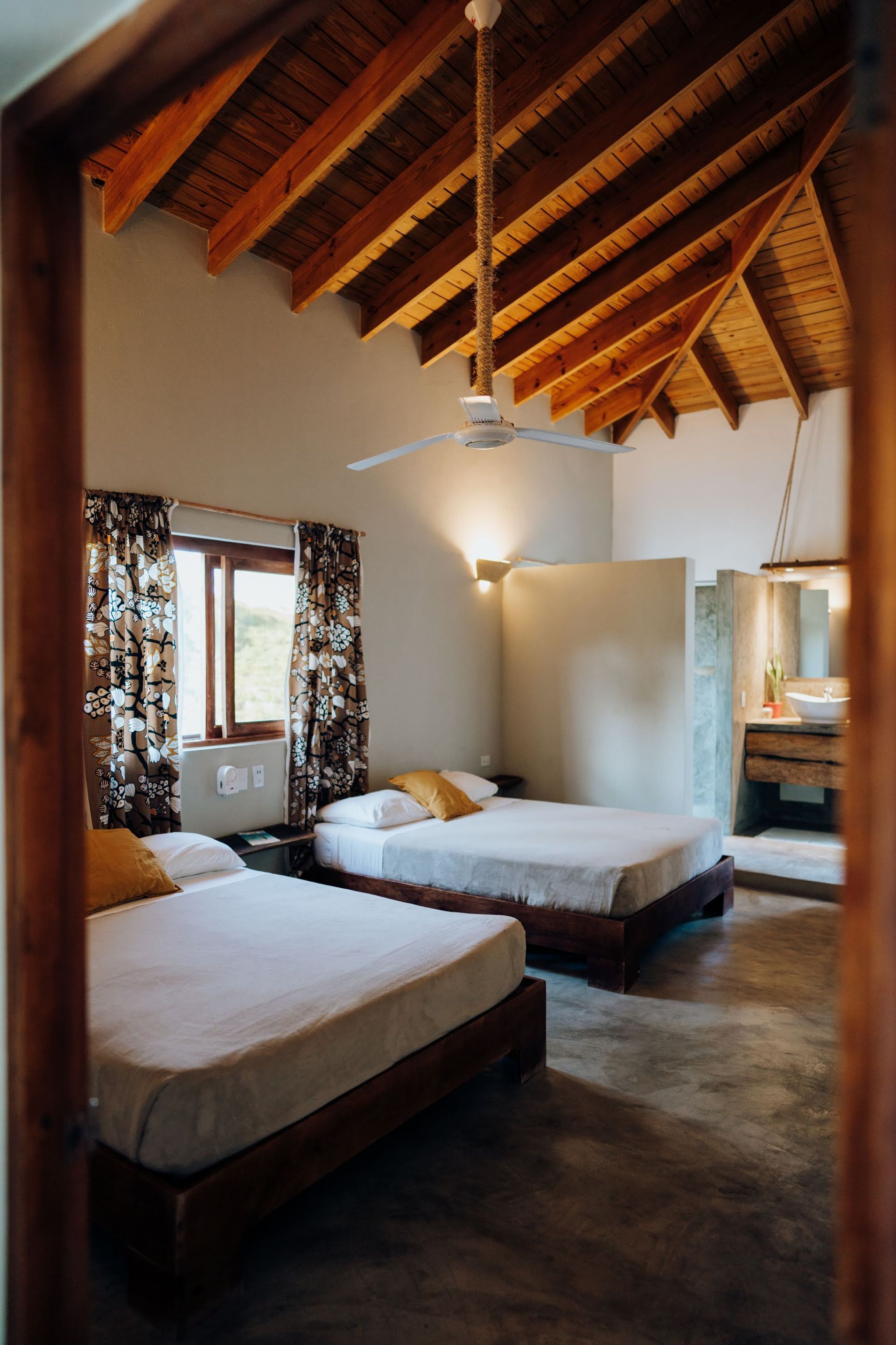 Bedroom with two beds, wooden ceiling, and floral curtains.