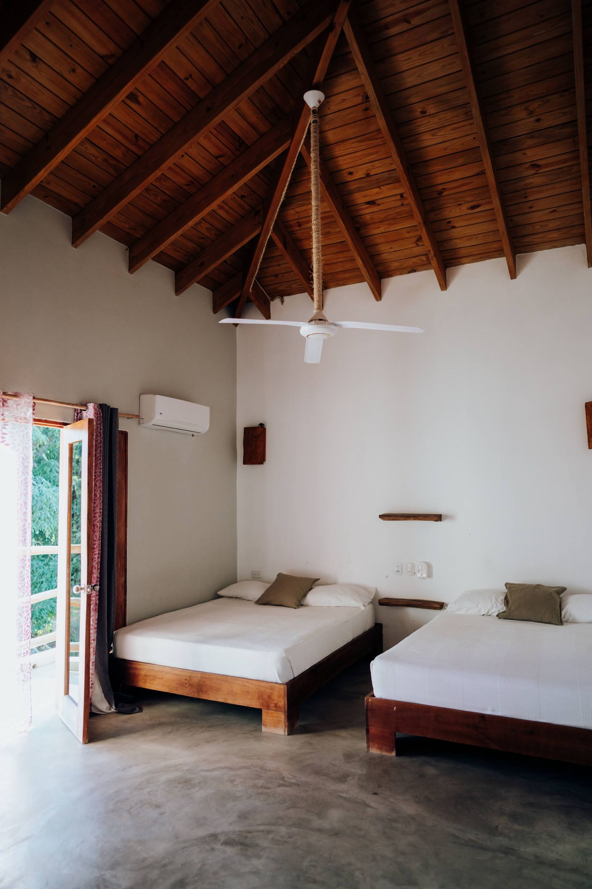 Bedroom with two beds, wooden ceiling, and open door to the outside.