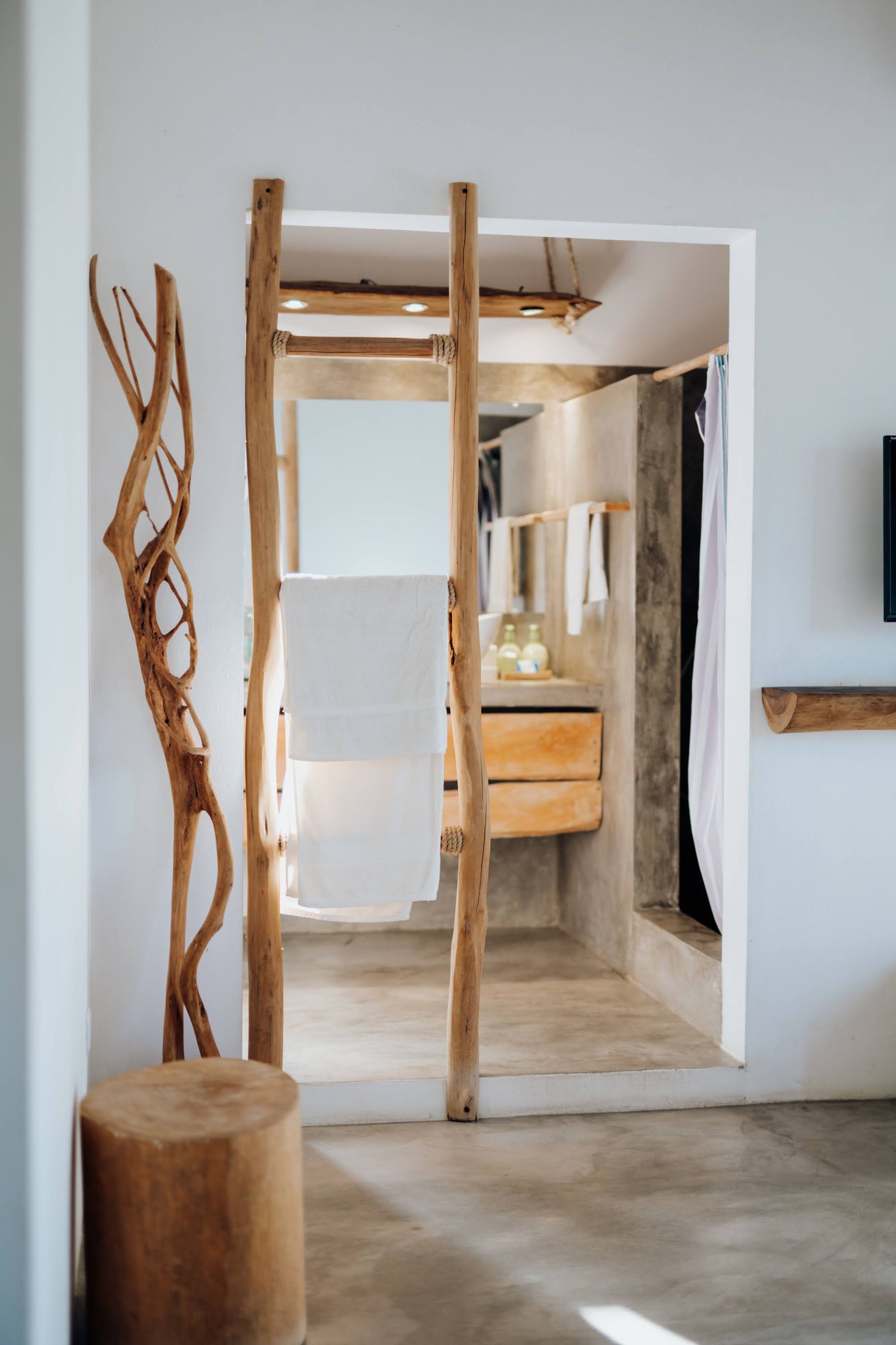 Rustic bathroom with a wooden ladder for towels, stump stool, and natural decor.