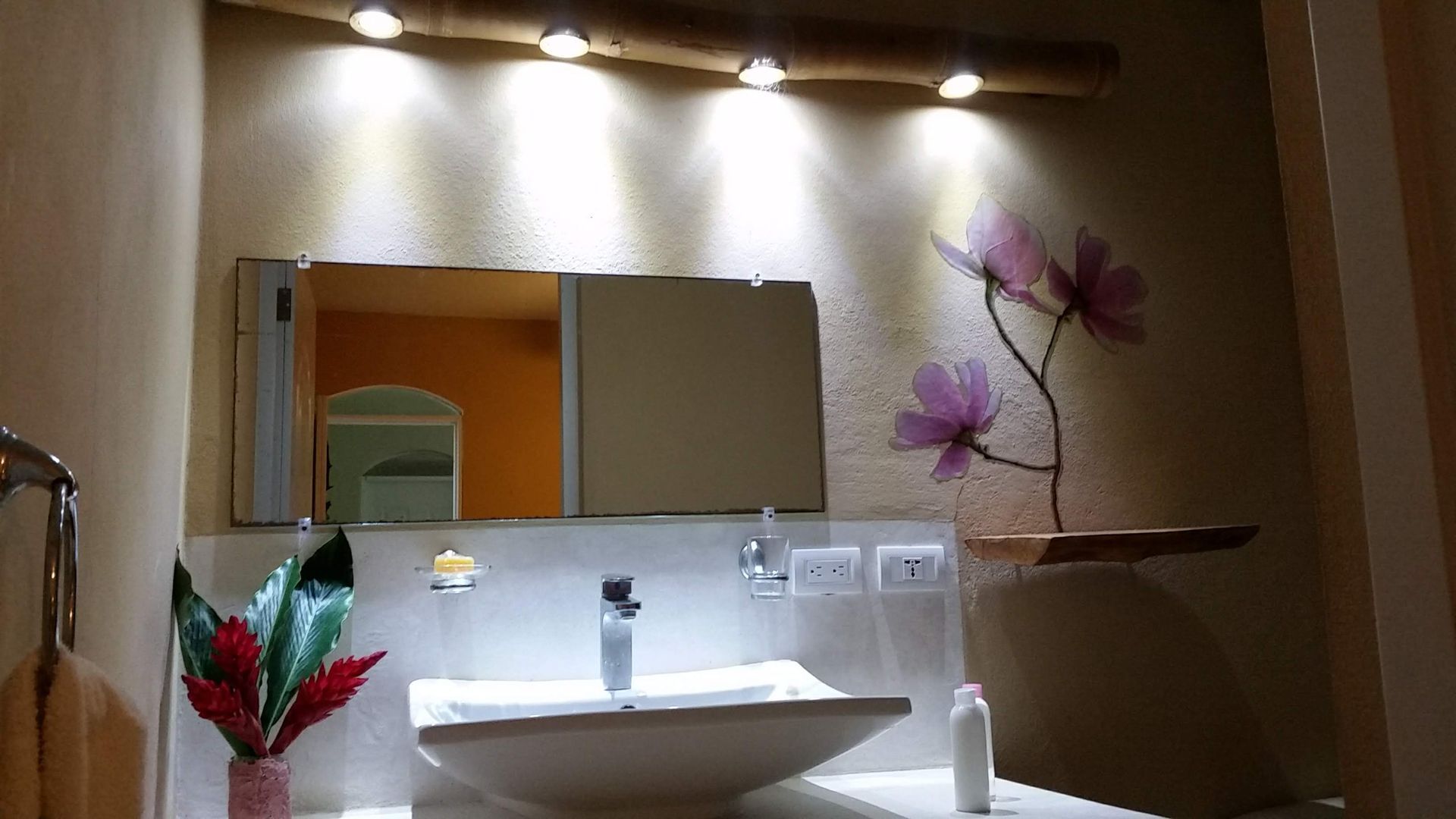 Bathroom with sink, mirror, and decorative flowers, under lights.