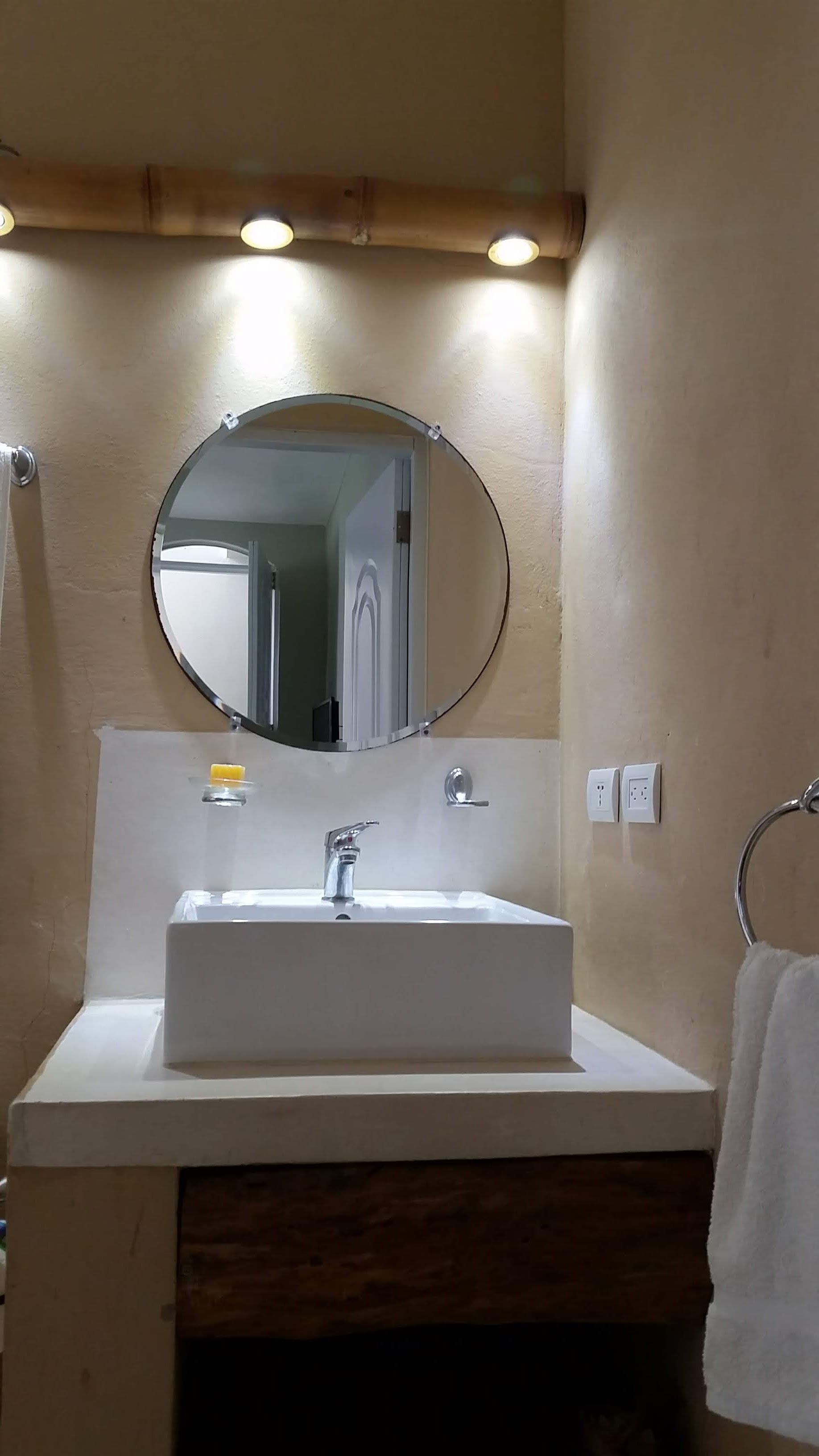 Bathroom with a rectangular white sink, round mirror, and towel rack.