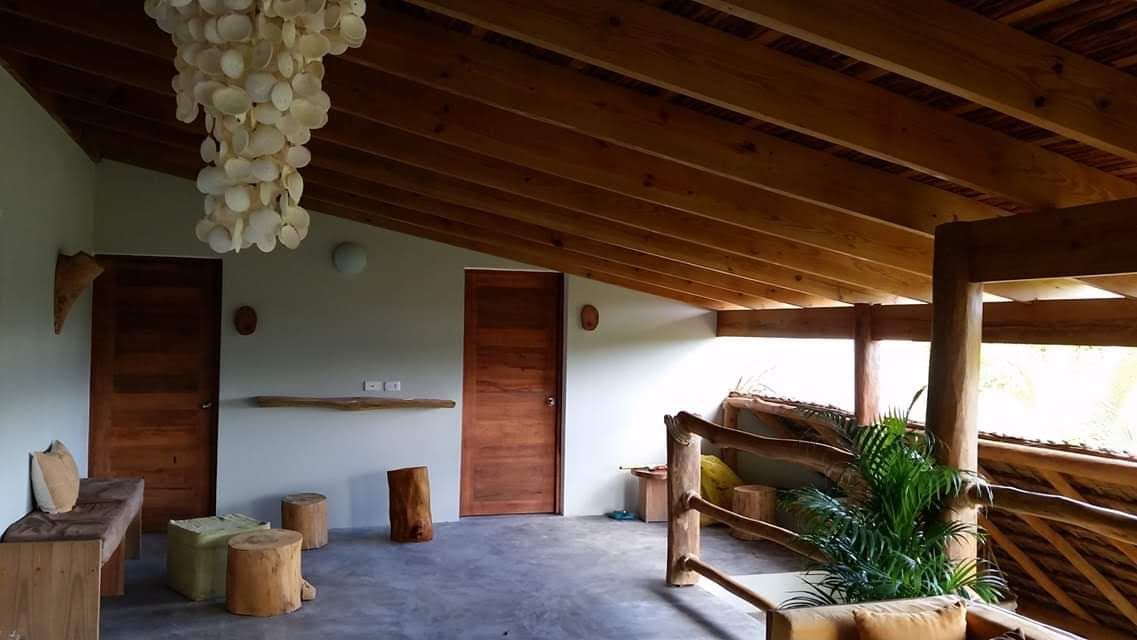 Veranda with wooden beams, railings, and doors, with a shell chandelier and tree stump seats.