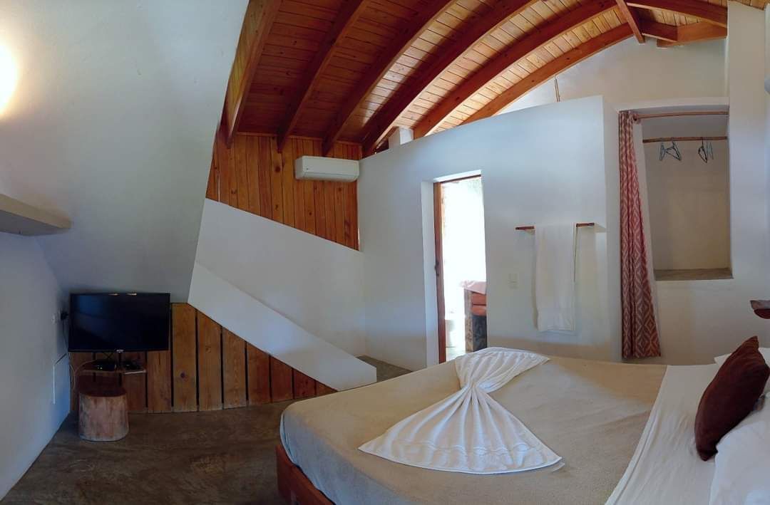 Bedroom with a wooden beamed ceiling, a bed with folded towel, and a television.
