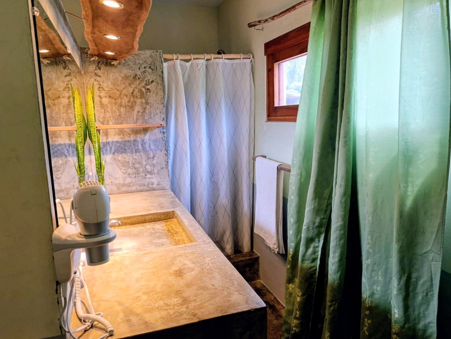 Bathroom with a concrete countertop, shower curtain, and green curtains.