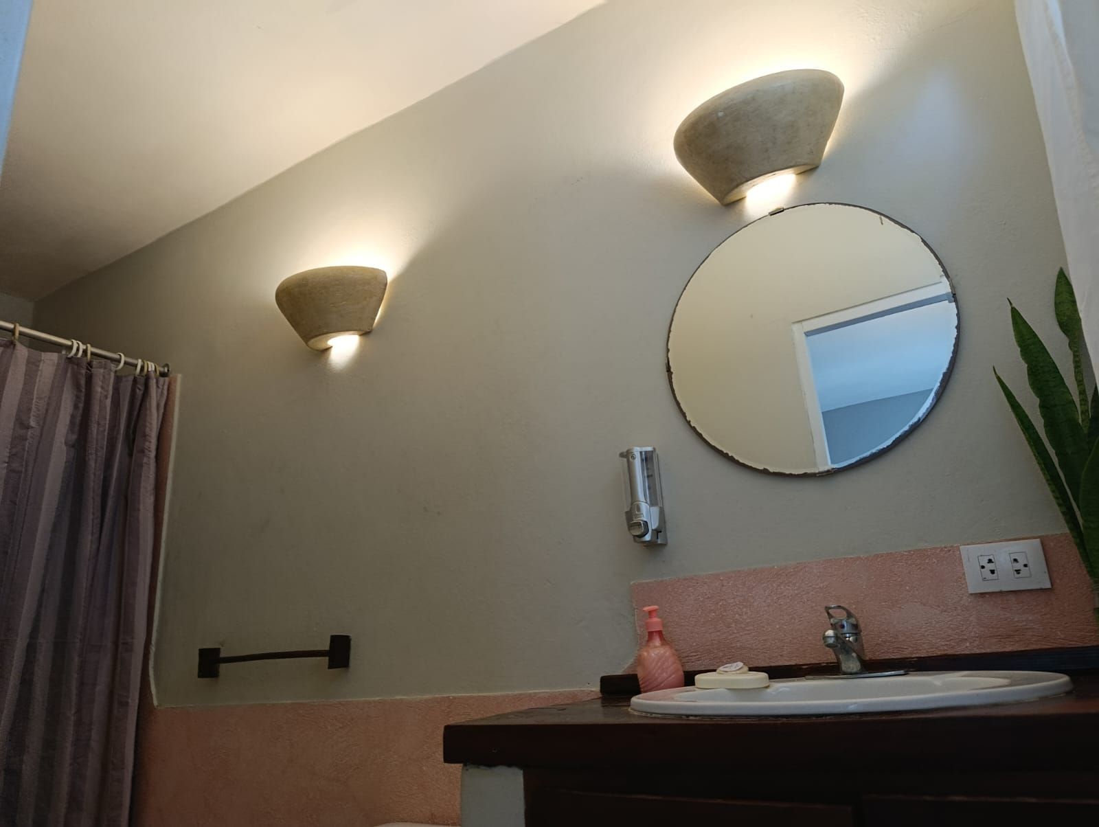 Bathroom with a round mirror, sconce lights, and a sink.