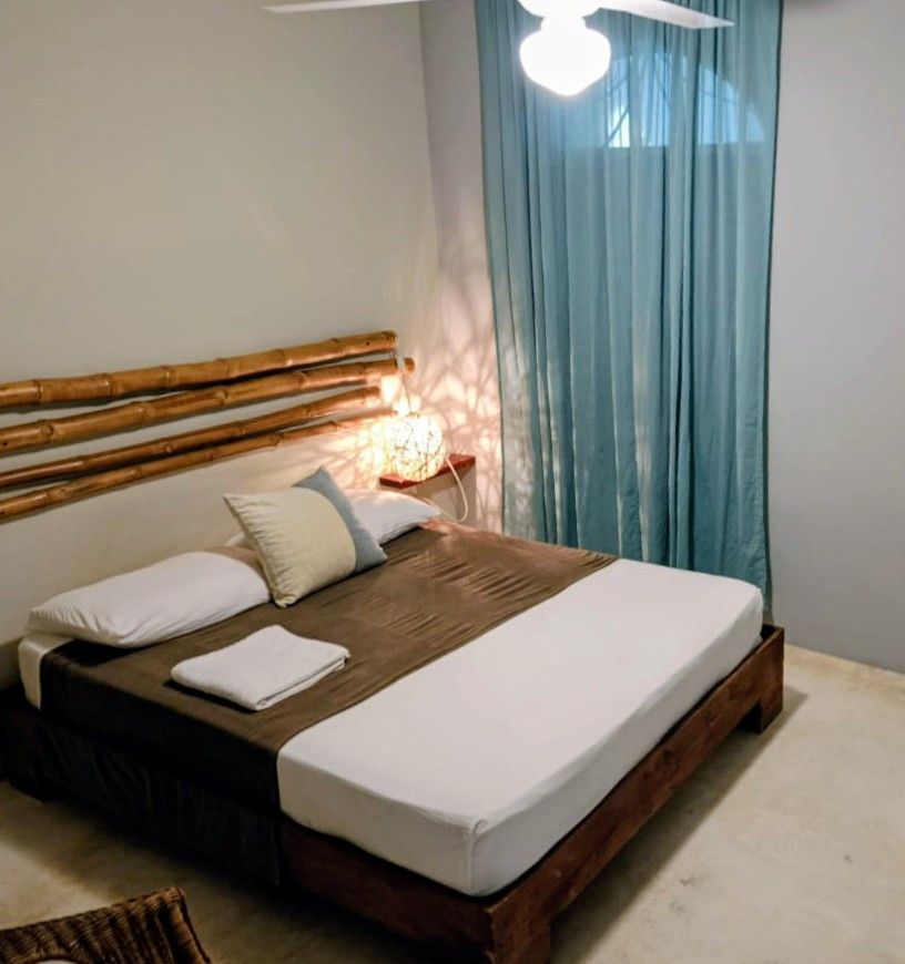 Bedroom with bed, bamboo headboard, white and brown bedding, light blue curtains.