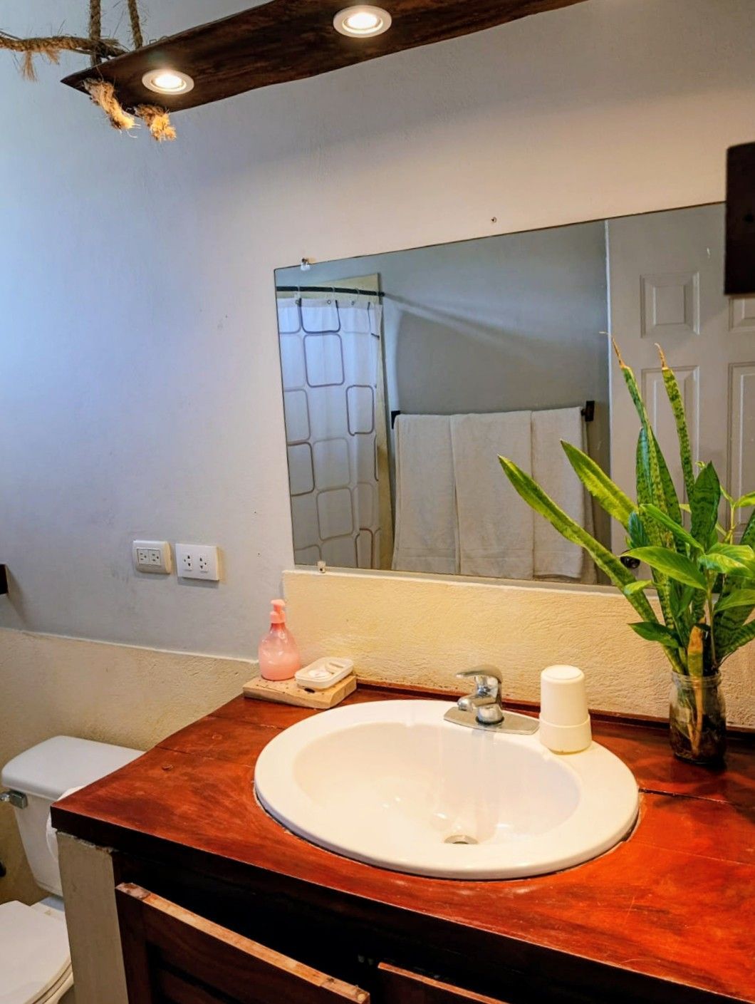 Bathroom with wood vanity, white sink, large mirror reflecting a shower.