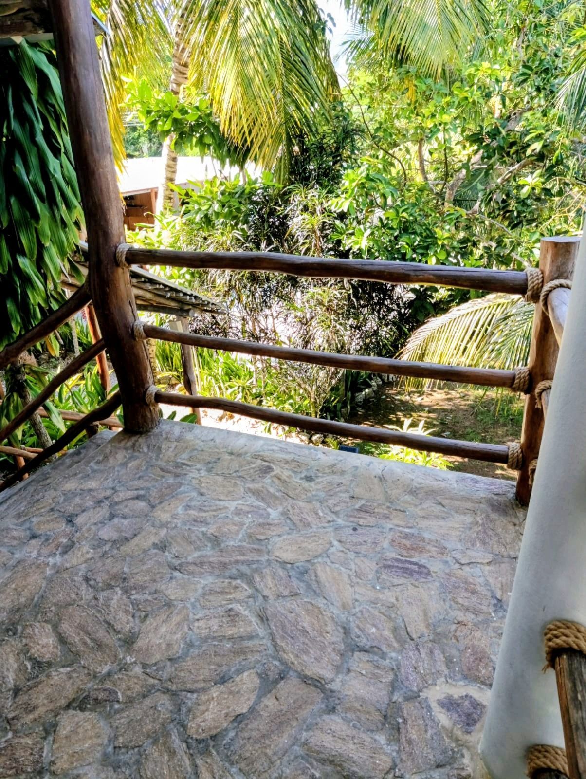 Stone patio with wooden railing overlooking lush green foliage.