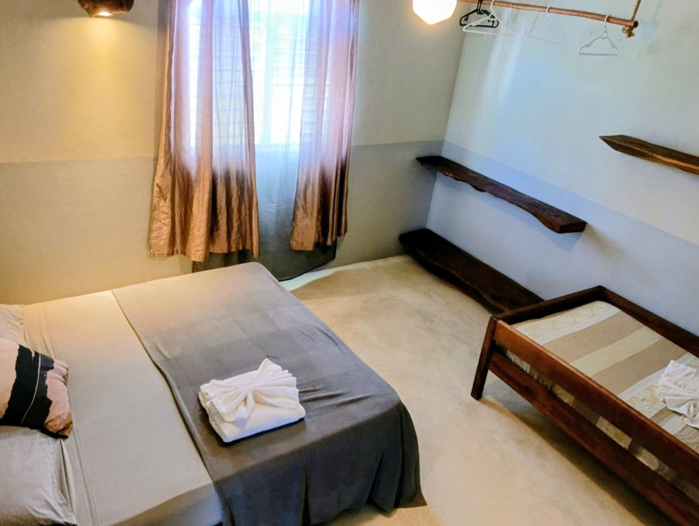 Bedroom with bed, single bed, shelves, and curtains. Walls are light gray and white.