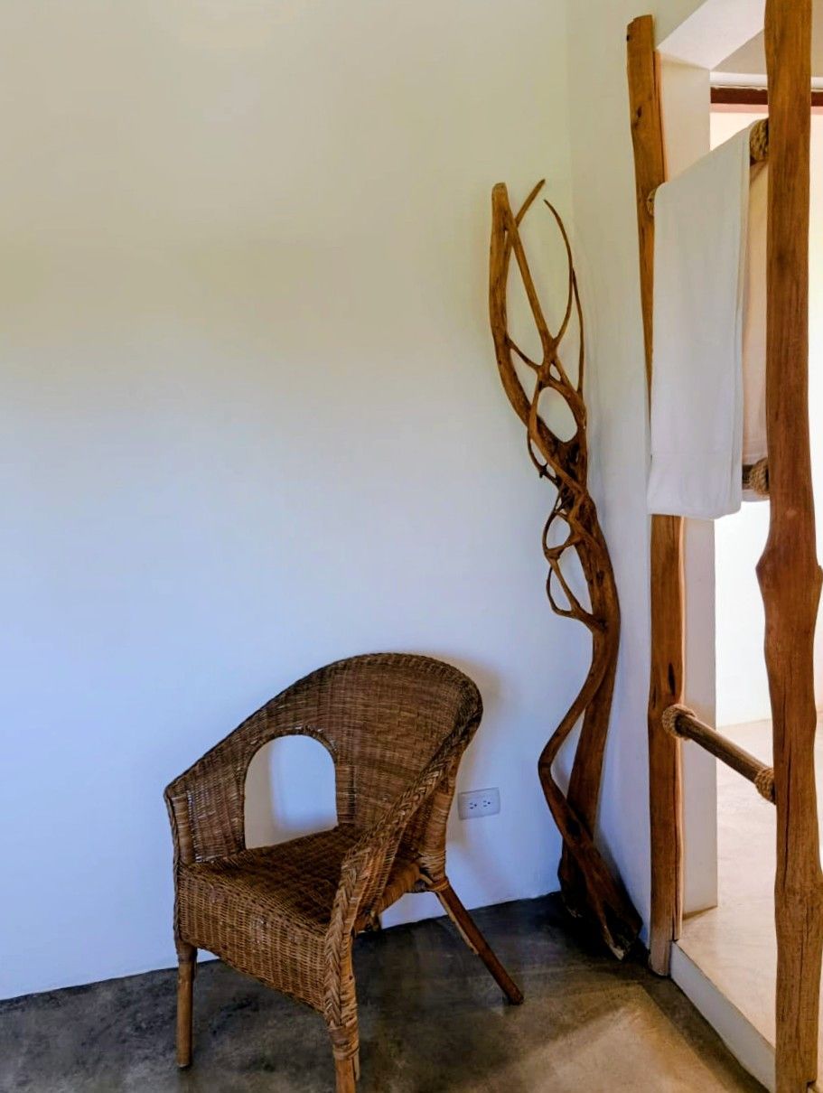Wicker chair next to a decorative driftwood and wooden towel rack against a white wall.