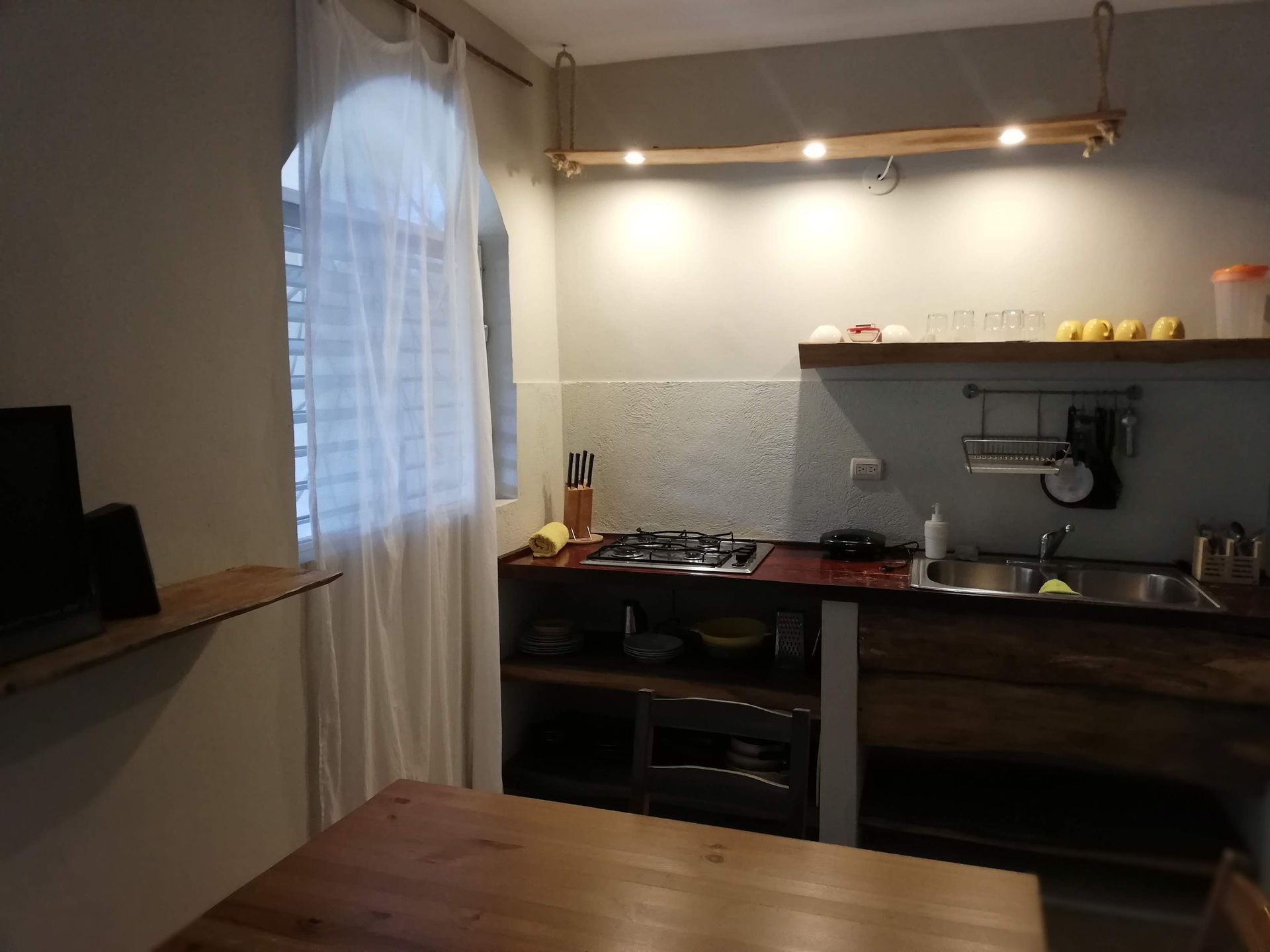 Kitchen with wooden cabinets, stovetop, and window with white curtains.