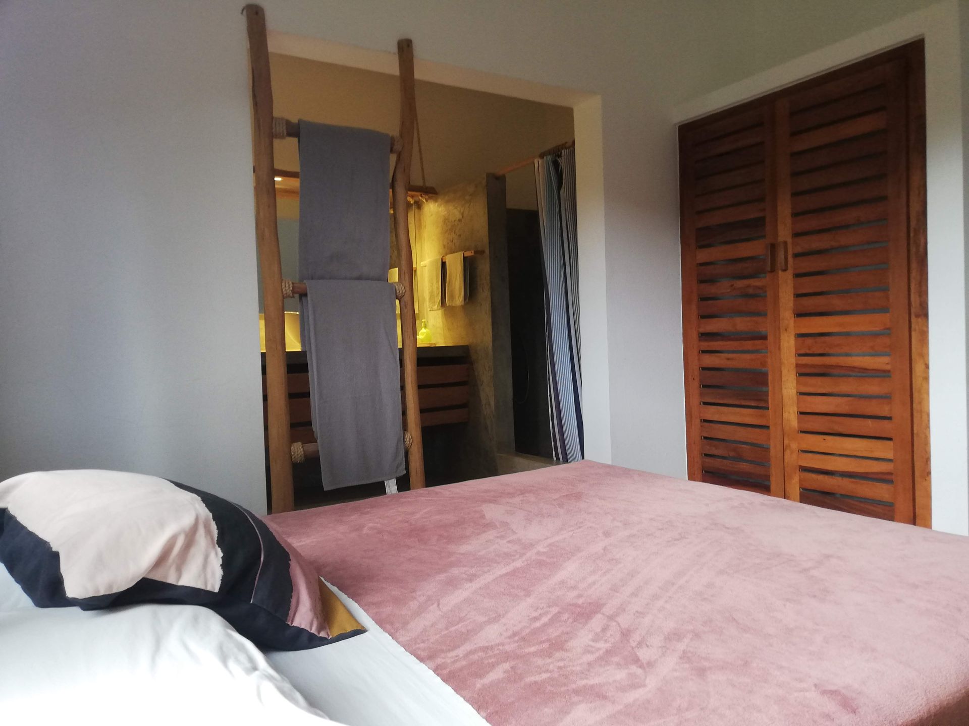Bedroom with a pink bed, wooden closet, and a towel ladder leading to a bathroom.