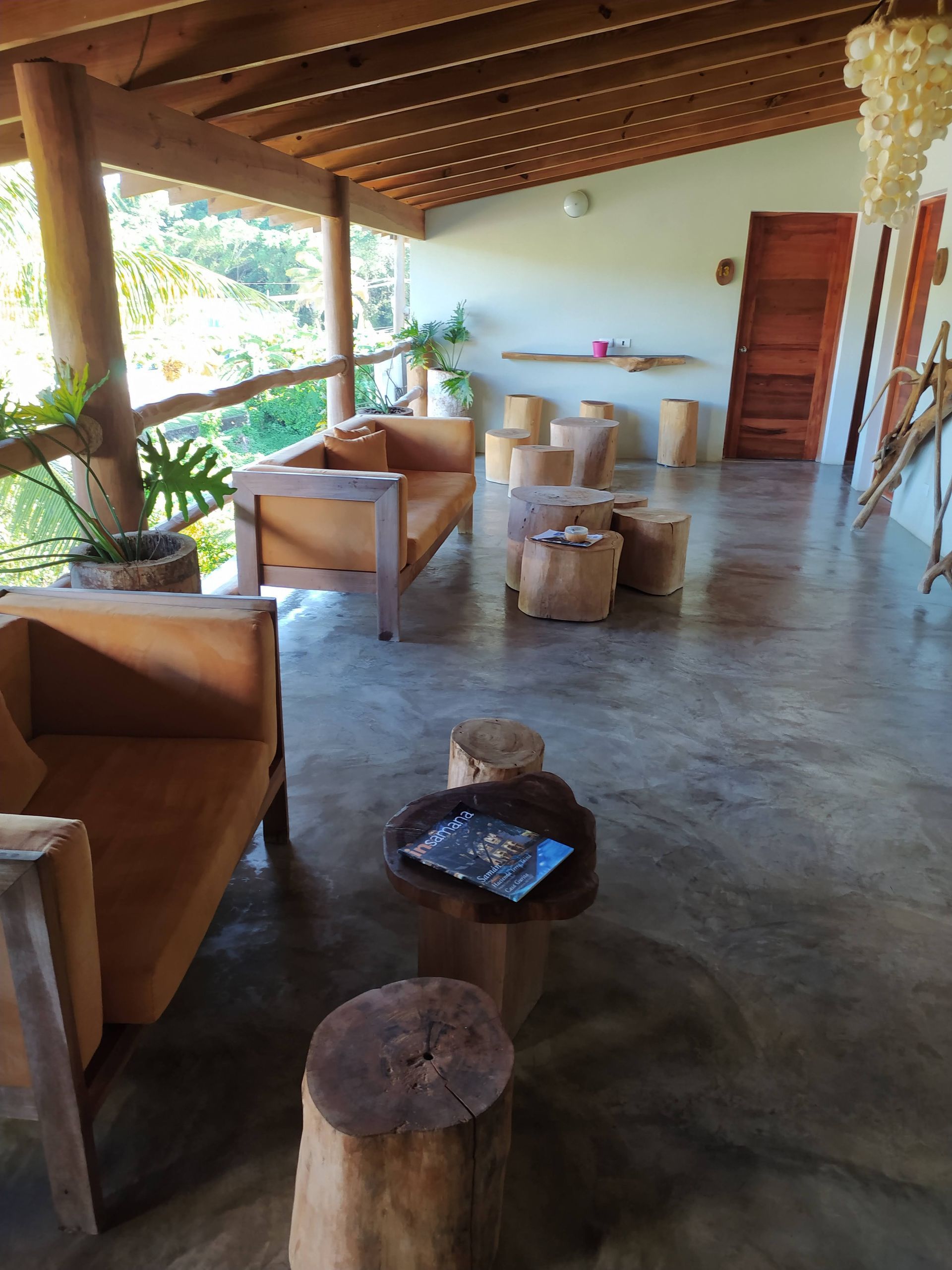 Covered porch with wood furniture, trees in background, concrete floor.