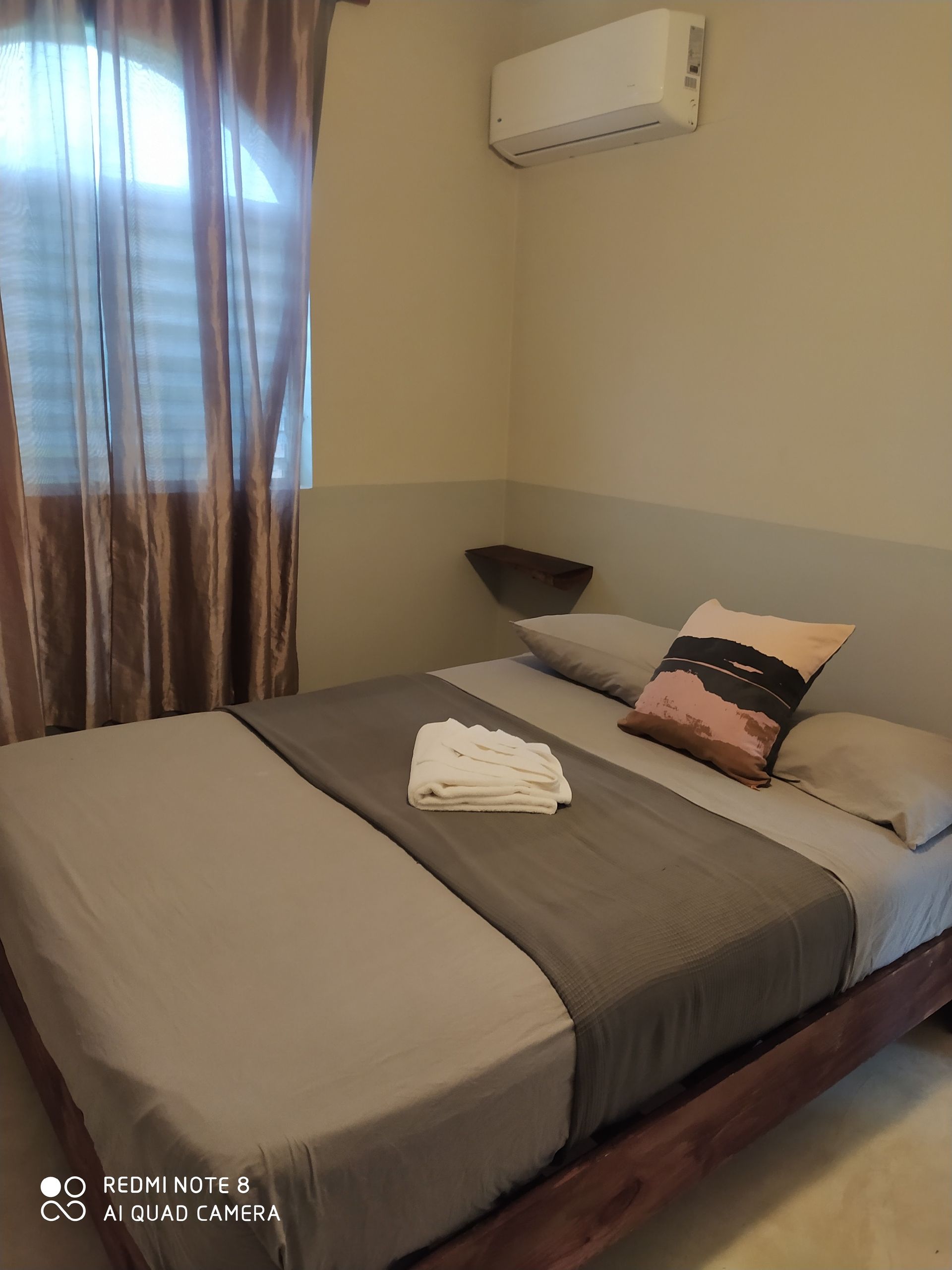 Bedroom with bed, pillow, towel, window with curtains, and air conditioner.