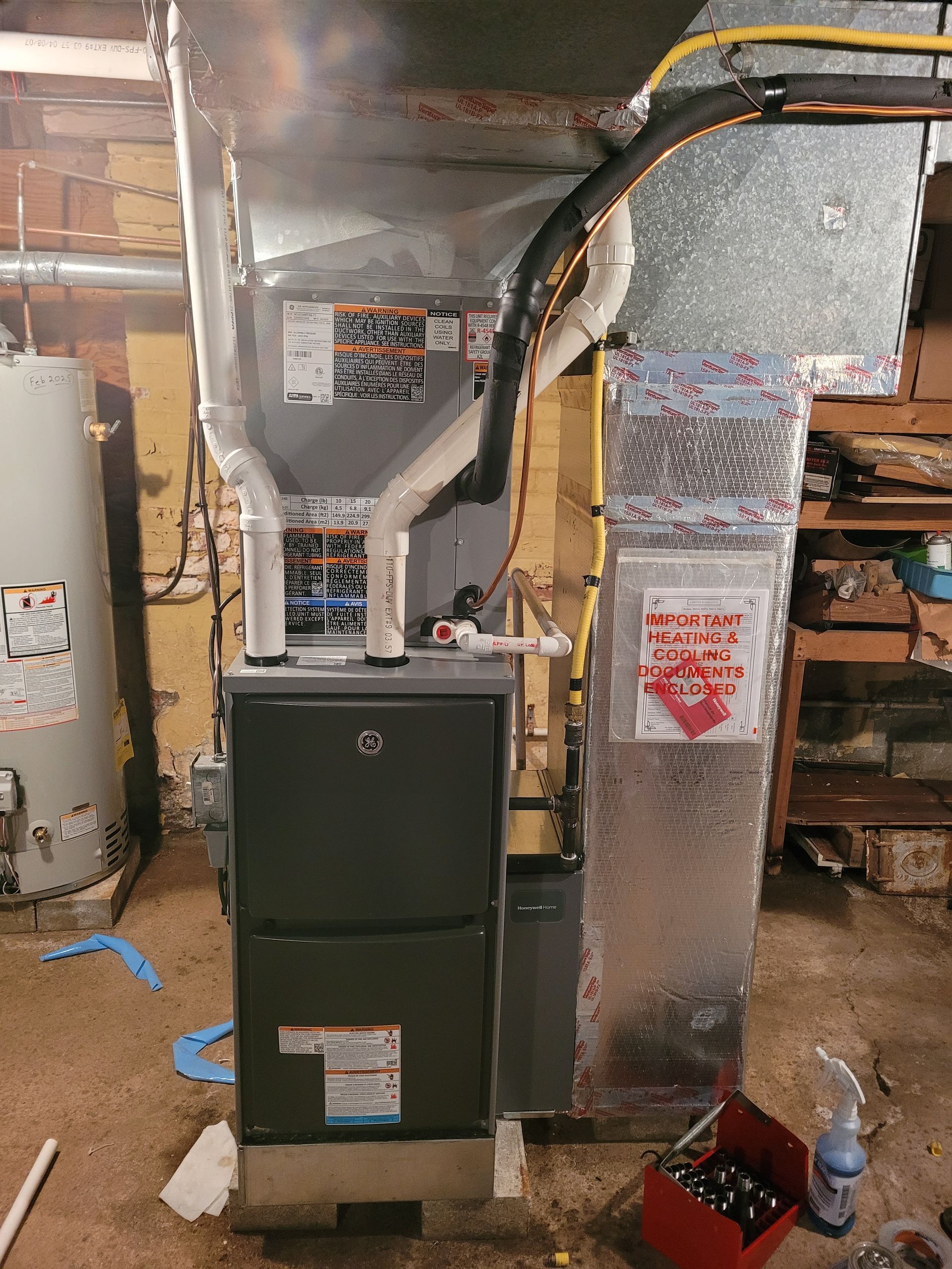 Furnace and ductwork in a utility room, with insulated air ducts and a red warning label.