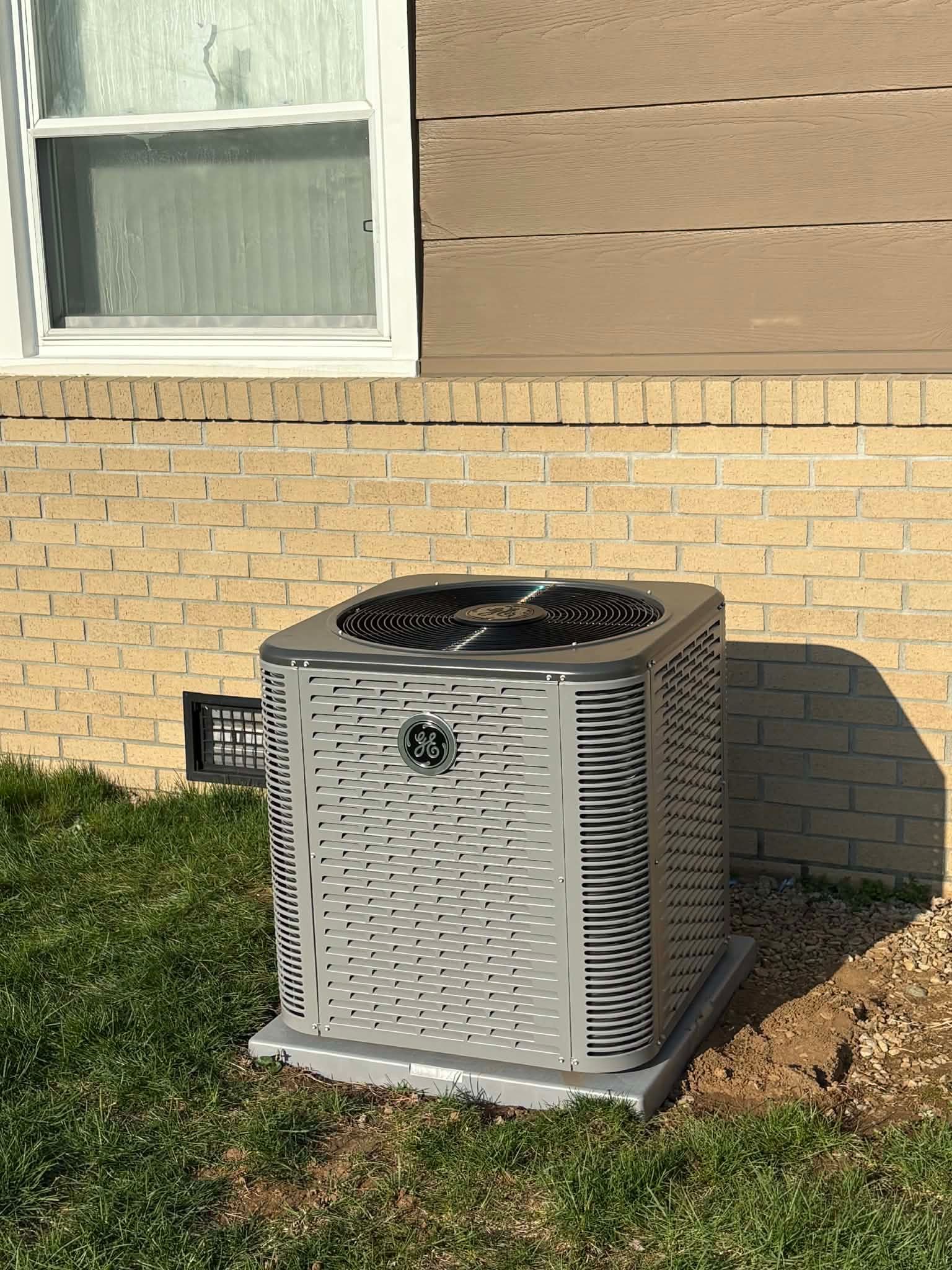 A technician uses pliers to work on the external copper pipe connections of a white air conditioning unit.
