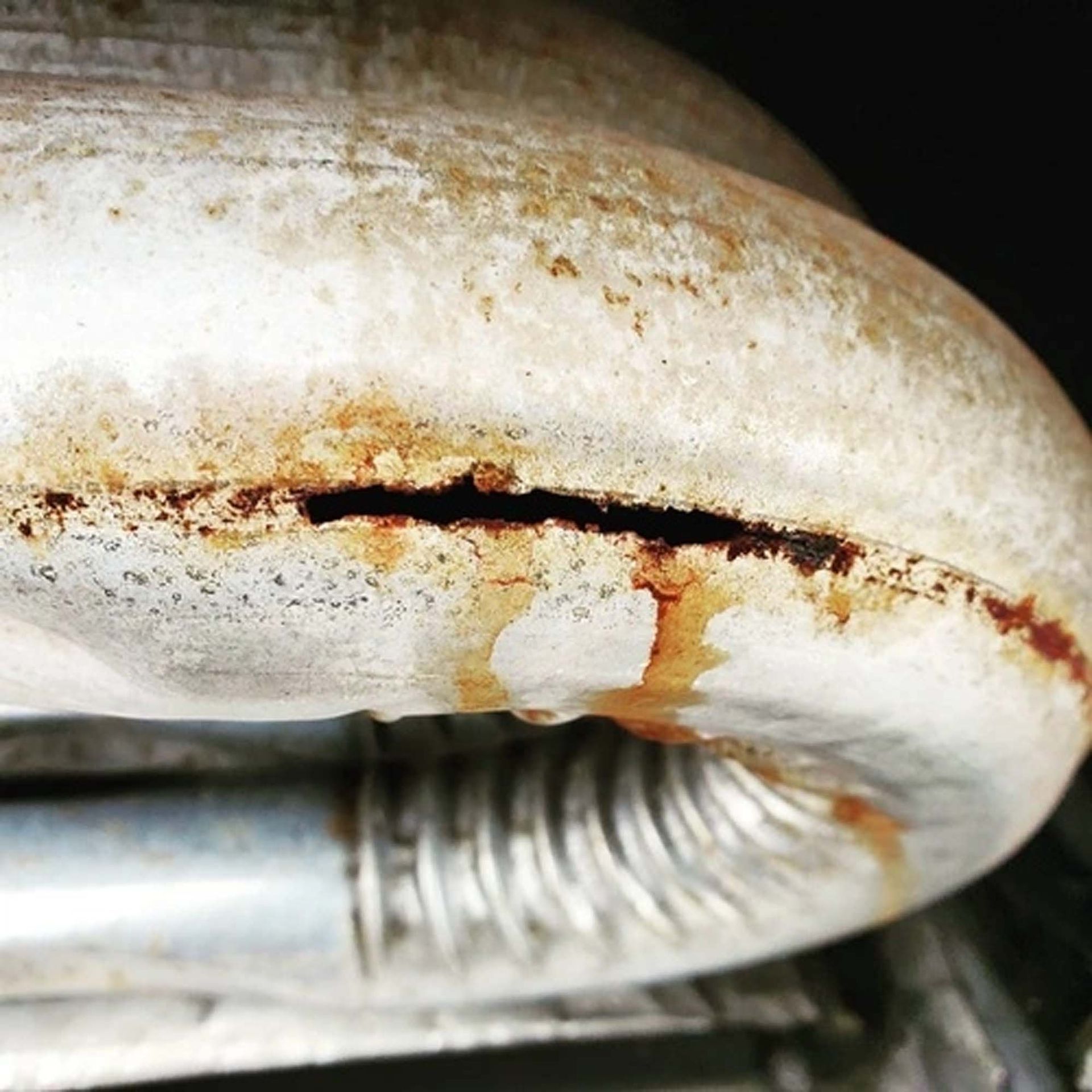 Rusty cracked white metal pipe with a small welded repair and visible corrosion