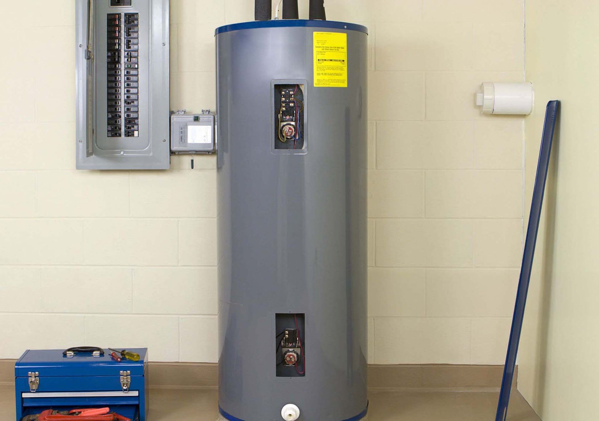 A gray furnace unit with white PVC venting and a metal duct, positioned next to a water heater in a utility closet.