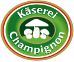 Logo für Käserel Champignon, einen Hersteller von Pilzkäse, mit Pilzen und Text auf einem grün-braunen runden Abzeichen.