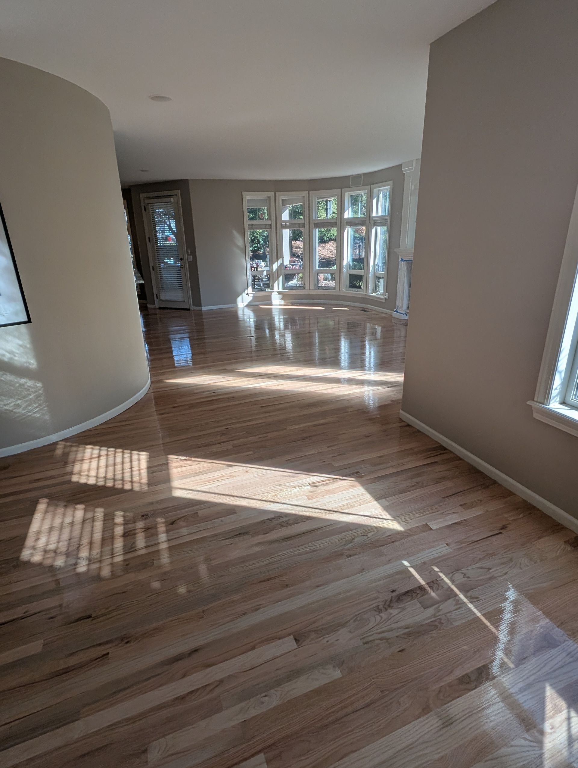 Person sanding a wooden floor with a handheld sander in a sunlit room.