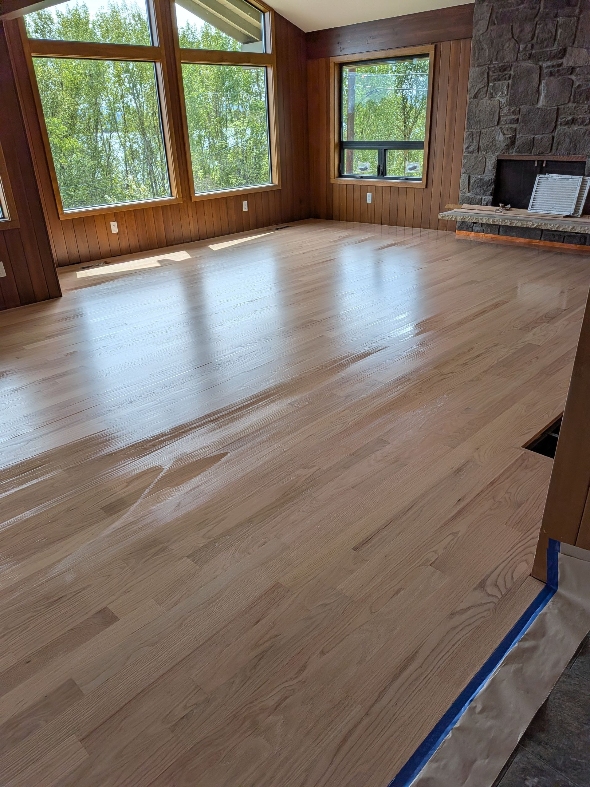Hardwood floor refinishing in progress showing raw sanded wood beside finished surface, Southern Oregon.