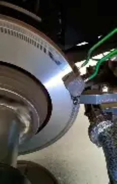 Close-up of a circular metal machine part with green wires and a gloved hand working on it