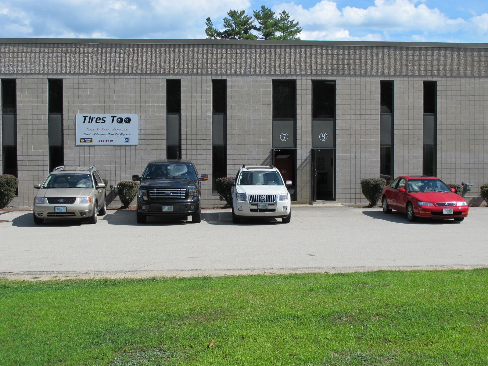 Four cars parked in front of a gray commercial building with a sign for a tax office.