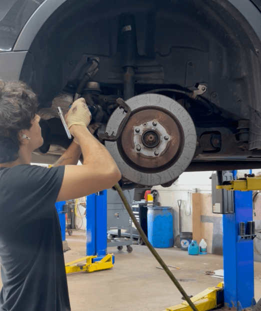 Mechanic working on a car’s front brake assembly in an auto repair shop, wheel removed on a lift