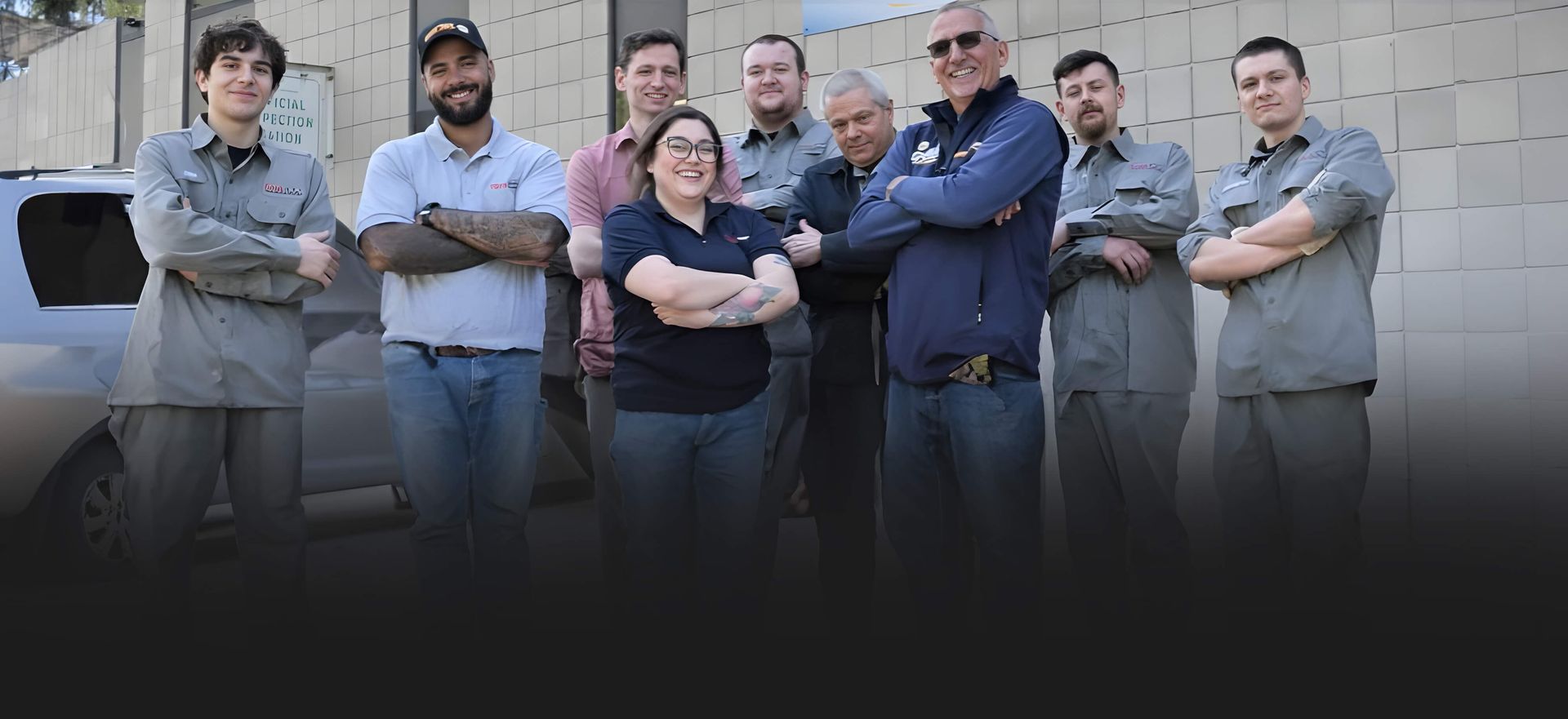 Group of six people standing outdoors with arms crossed in front of a building, posing for a photo.
