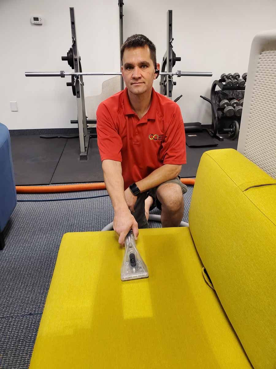 A man in a red shirt is cleaning a yellow couch