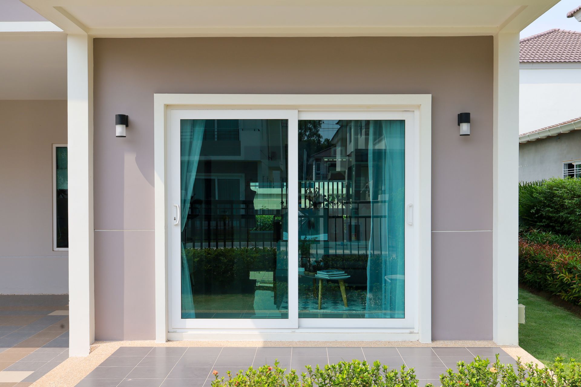 Modern house patio with large sliding glass doors and beige trim, flanked by wall lights.