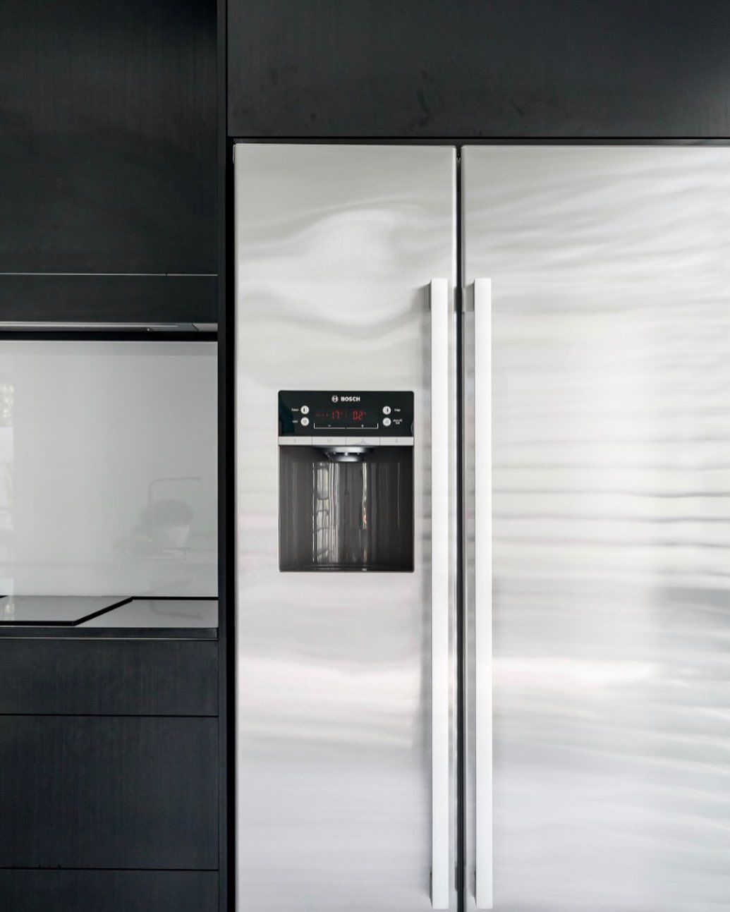 A stainless steel refrigerator in a kitchen with black cabinets