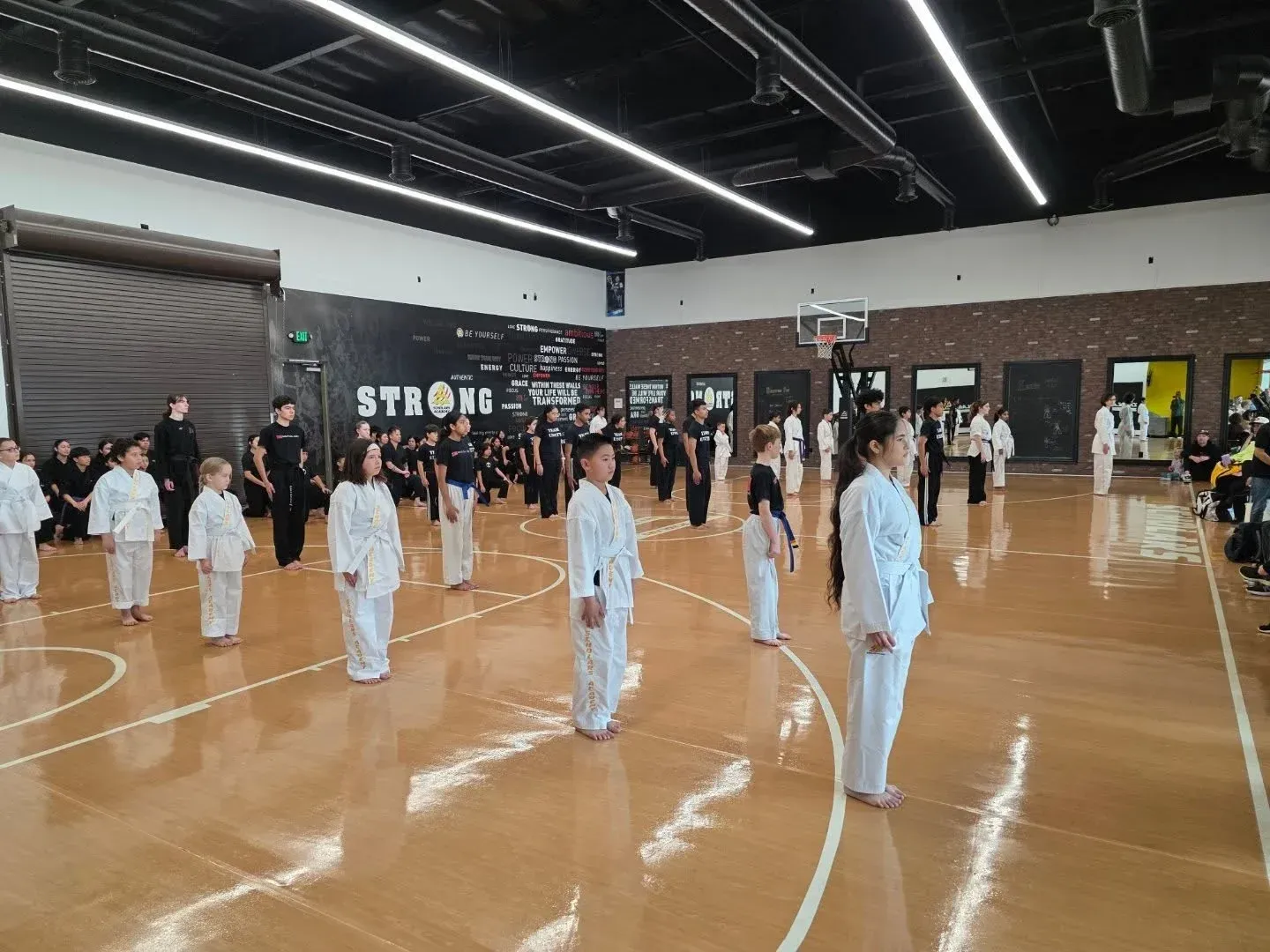 Children in white uniforms standing in rows in a gymnasium during a karate class