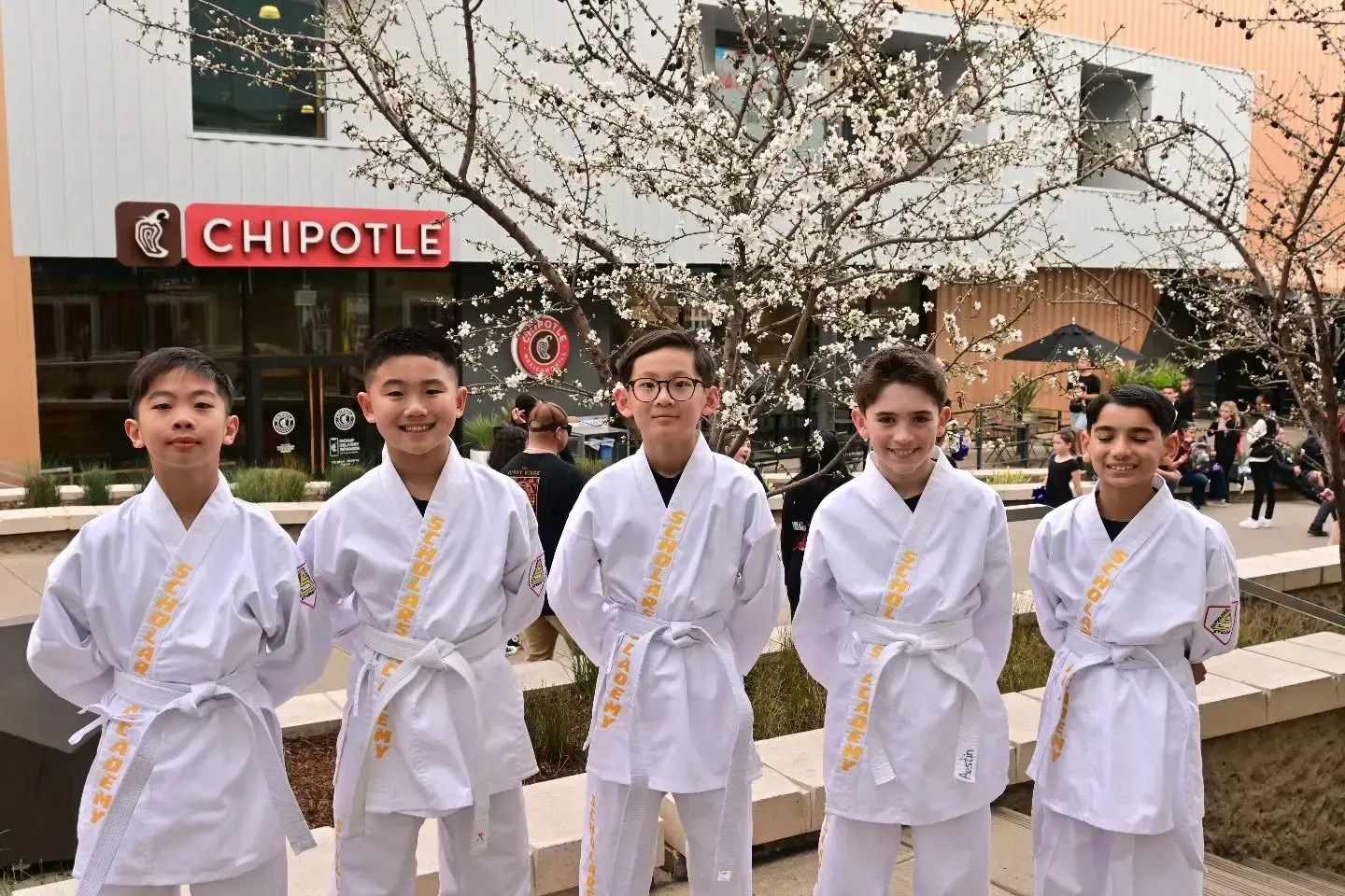 Five people in white martial arts uniforms standing outside a Chipotle restaurant