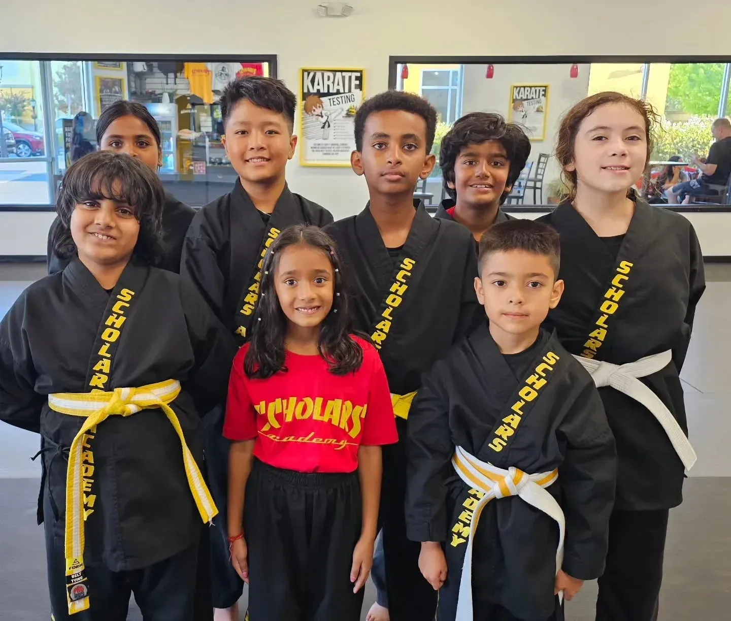Group of children in martial arts uniforms and sashes posing together indoors, smiling at the camera