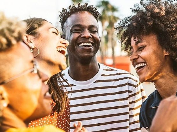 A diverse group of four people laughing together outdoors, viewed in a close-up shot.