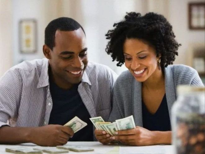 Two people sitting at a table smiling while counting stacks of cash.