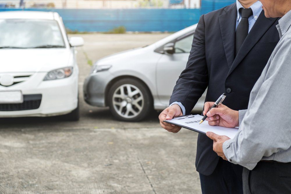 A man in a suit is holding a clipboard in front of two cars. — East Maitland Body Repairs in East Maitland, NSW