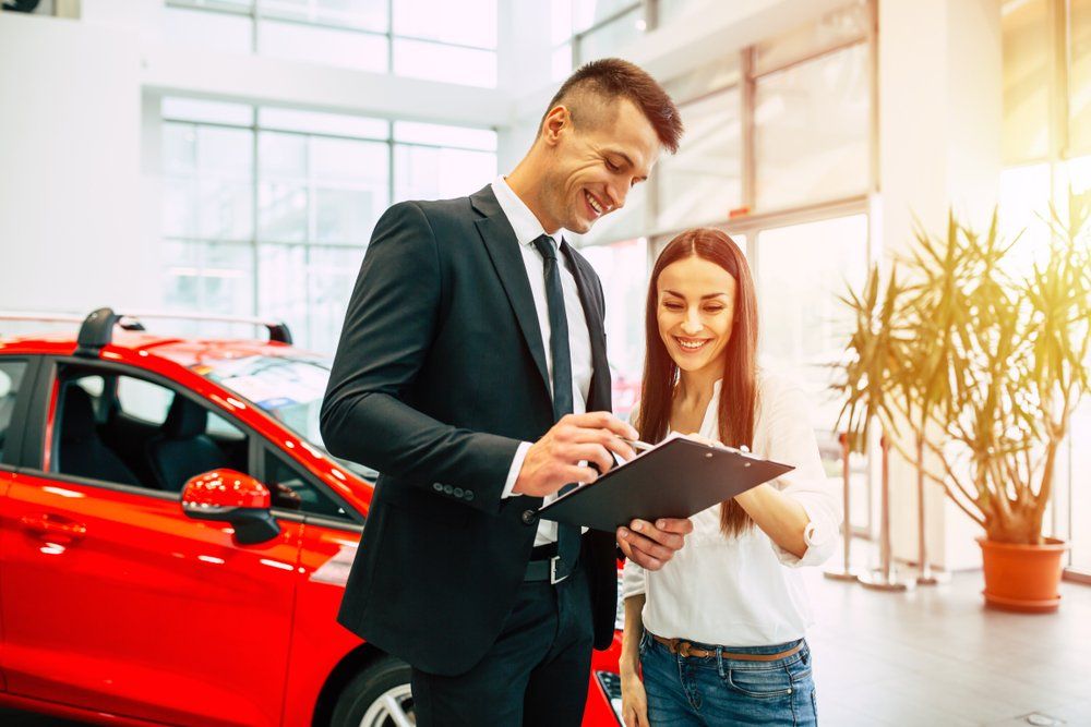A Man and A Woman Are Looking at A Clipboard in A Car Showroom — East Maitland Body Repairs in East Maitland, NSW